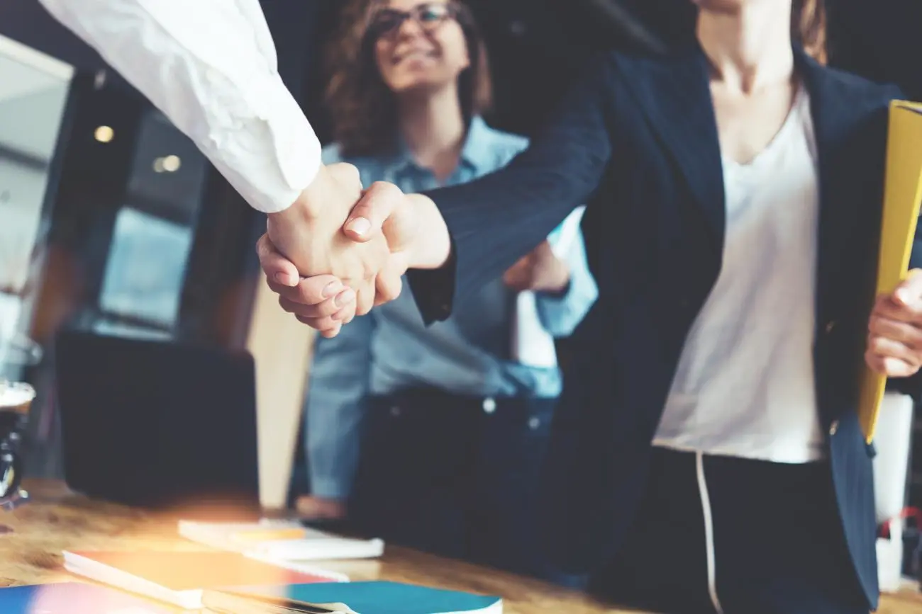 Two professionals shaking hands at a wooden table, discussing financial planning services from Statera Financial Planners.