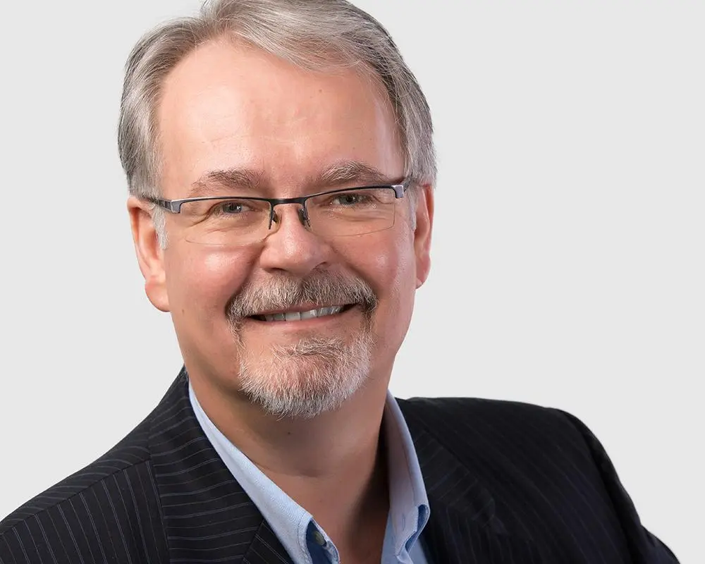 Greg MacIntosh, CFP®, CLU®, in a dark pinstripe suit, smiling professionally.