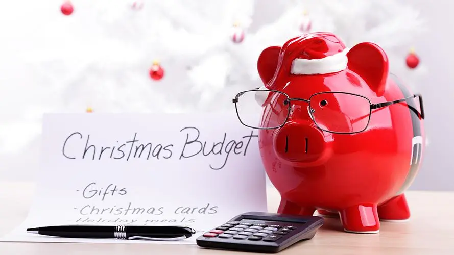 Red piggy bank with glasses and Santa hat, calculator, pen, and "Christmas Budget" list by Statera Financial Planners.