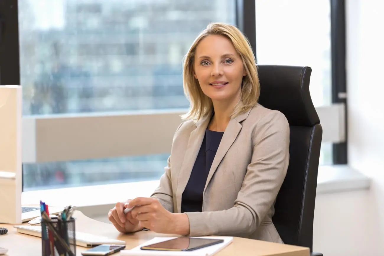 Professional woman at a desk in a bright office, using a laptop and tablet, promoting Statera Financial Planners' services.