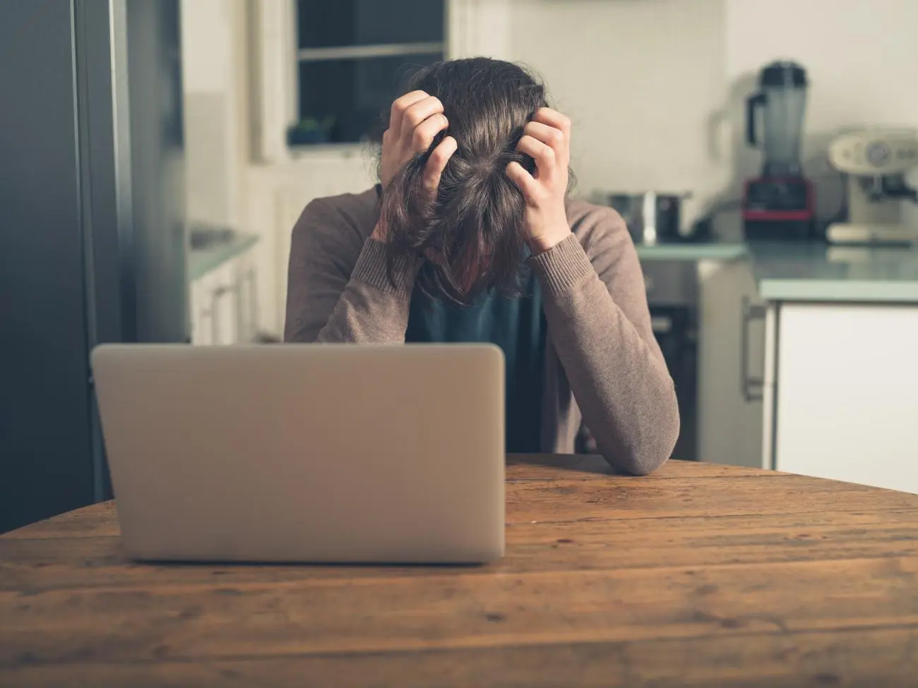 Person with tousled hair at a table with a laptop, showing financial anxiety, representing Statera Financial Planners.
