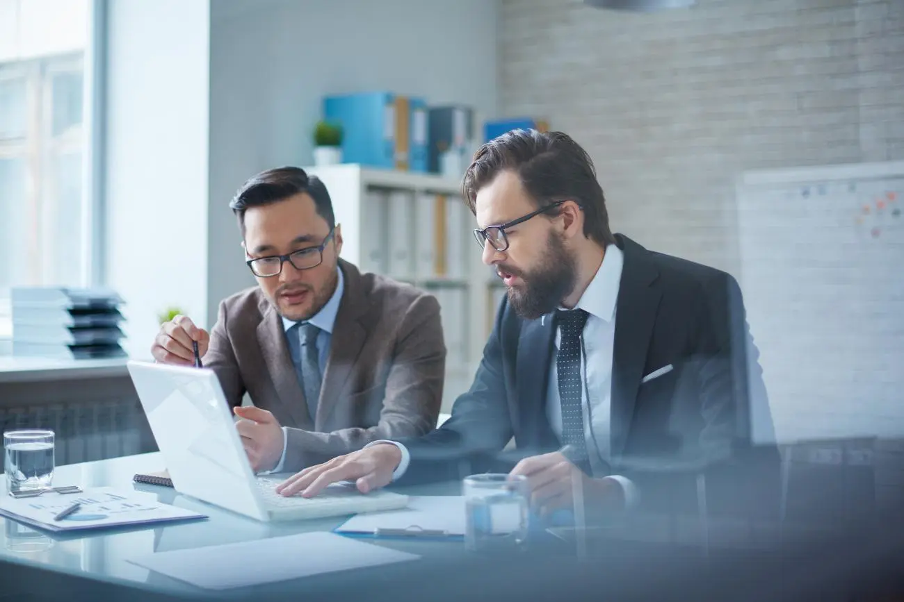 Two professionals discussing financial planning with laptop and documents at Statera Financial Planners’ modern office.